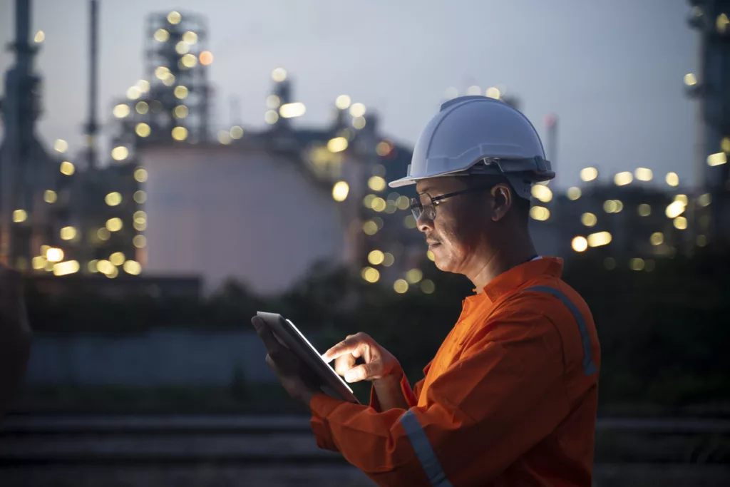 Engineer using Panni Management's ERP software on a tablet near oil refinery at night.