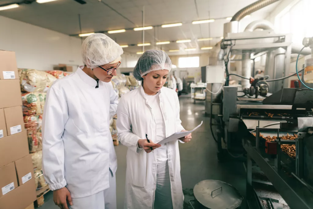Two quality professionals in white sterile uniforms checking quality of salt sticks while standing in food factory using Panni Management's Sage X3 ERP for food & Beverages industry