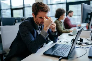 An exhausted Netsuite user sitting in front of his laptop computer in an office and considering to move to Sage X3 from Panni Management