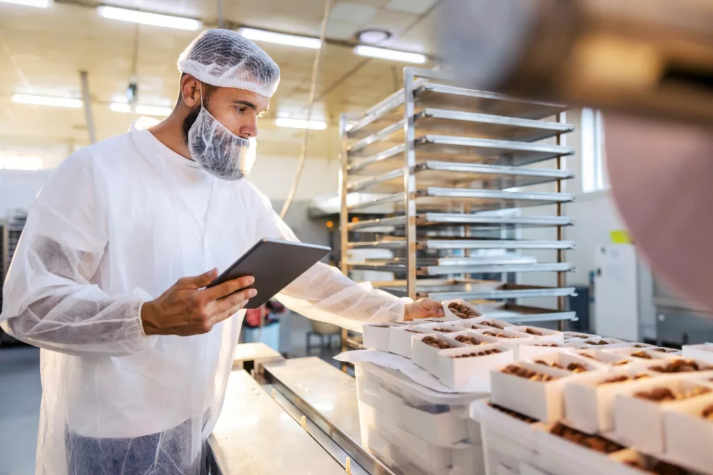 Panni Management's Sage X3 - Bakery ERP user in a sterile white uniform is holding the tablet and looking at collected cookies.