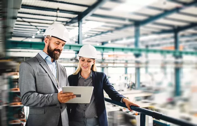 A portrait of a mature industrial man and woman engineer with tablet in a factory, working.